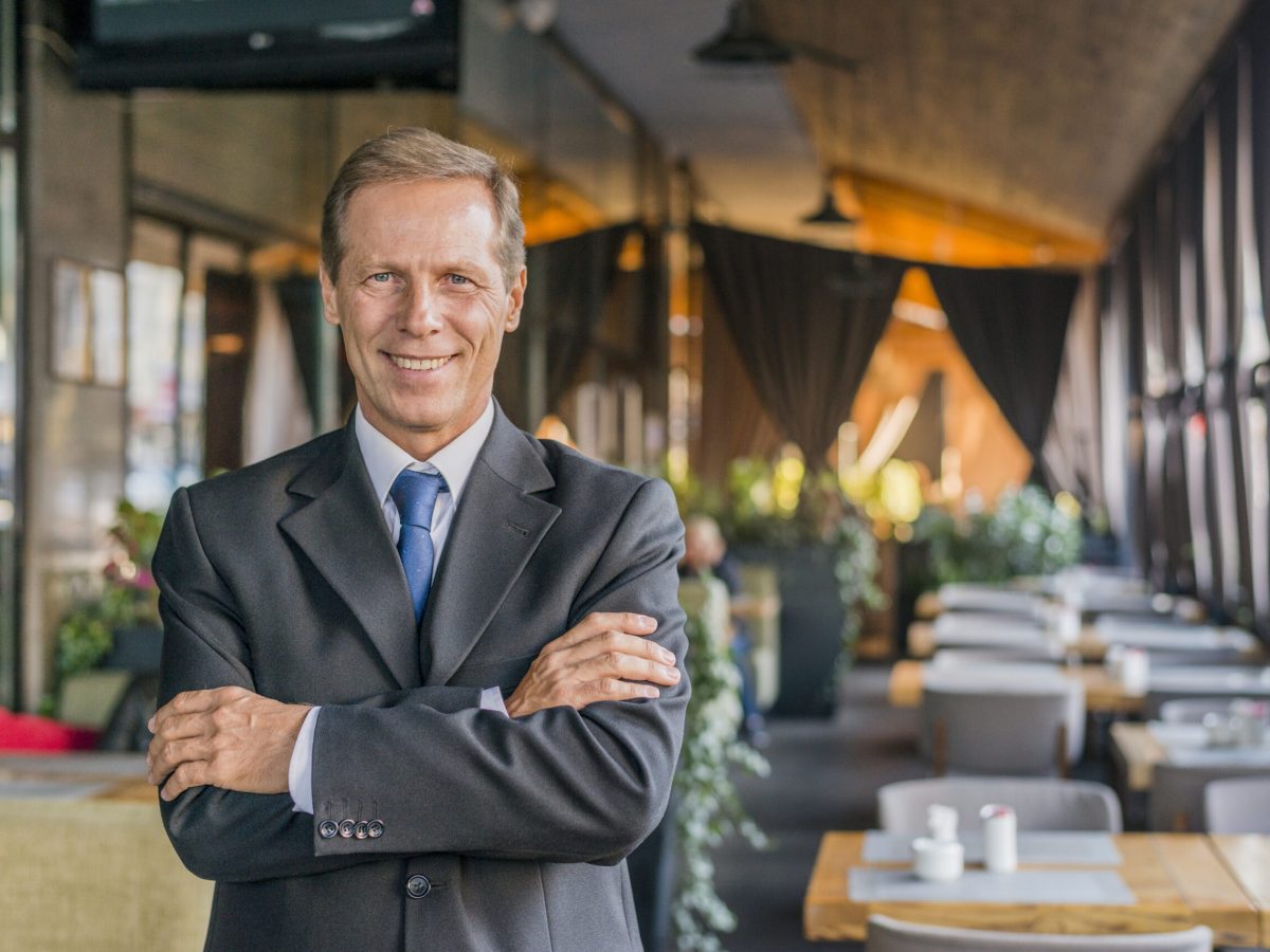 portrait-happy-successful-businessman-standing-restaurant-with-crossed-arm