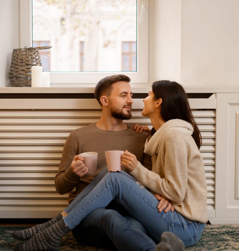 Romantic couple at home. An Attractive young woman and handsome man are enjoying spending time together while siting coddling with cups of tea in hands.
